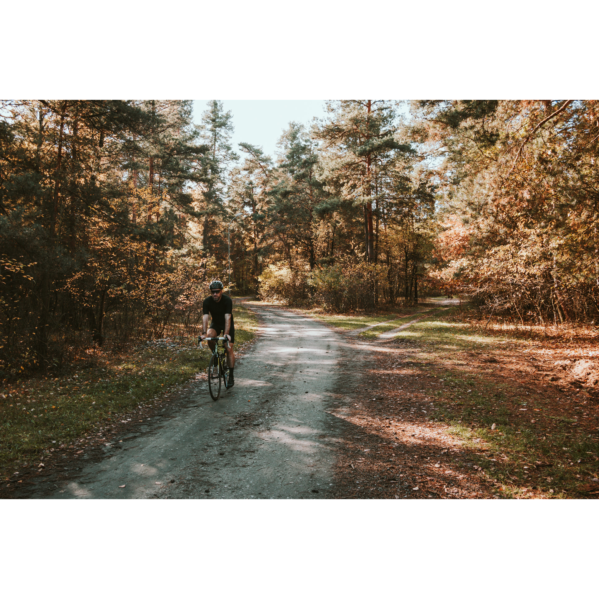 A cyclist in a black outfit, glasses and a helmet cycling along a sandy forest road