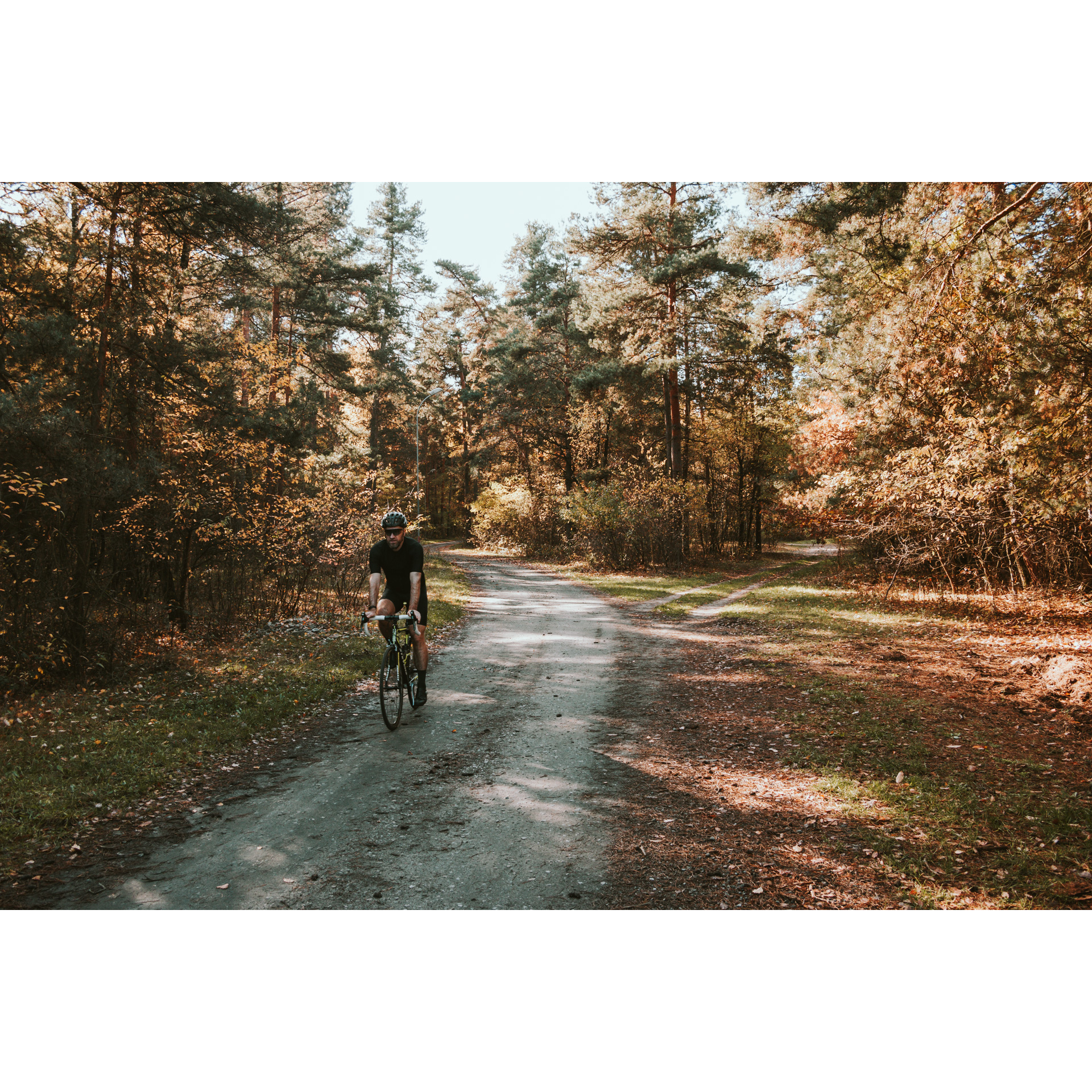 Rowerzysta w czarnym stroju, okularach i kasku jadący na rowerze piaszczystą drogą leśną