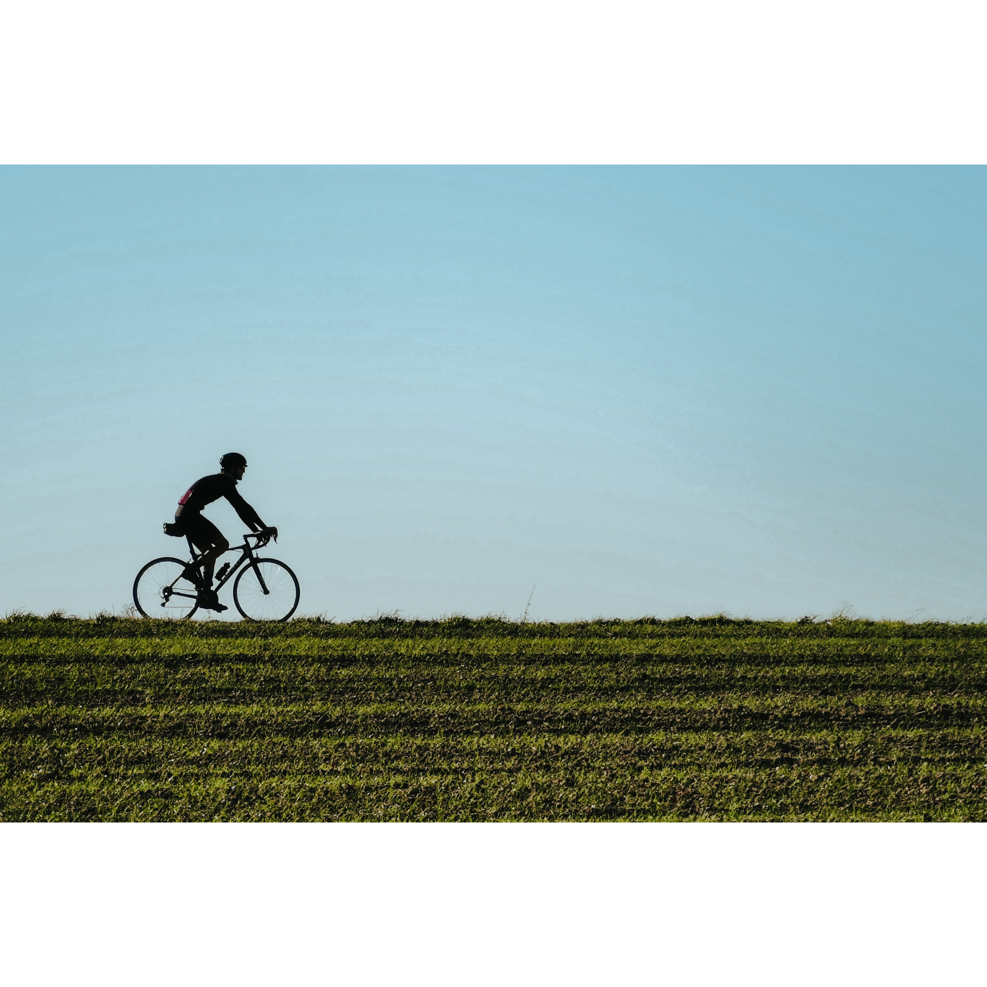 A cyclist in cycling clothes and a helmet riding along a green farmland against a blue sky