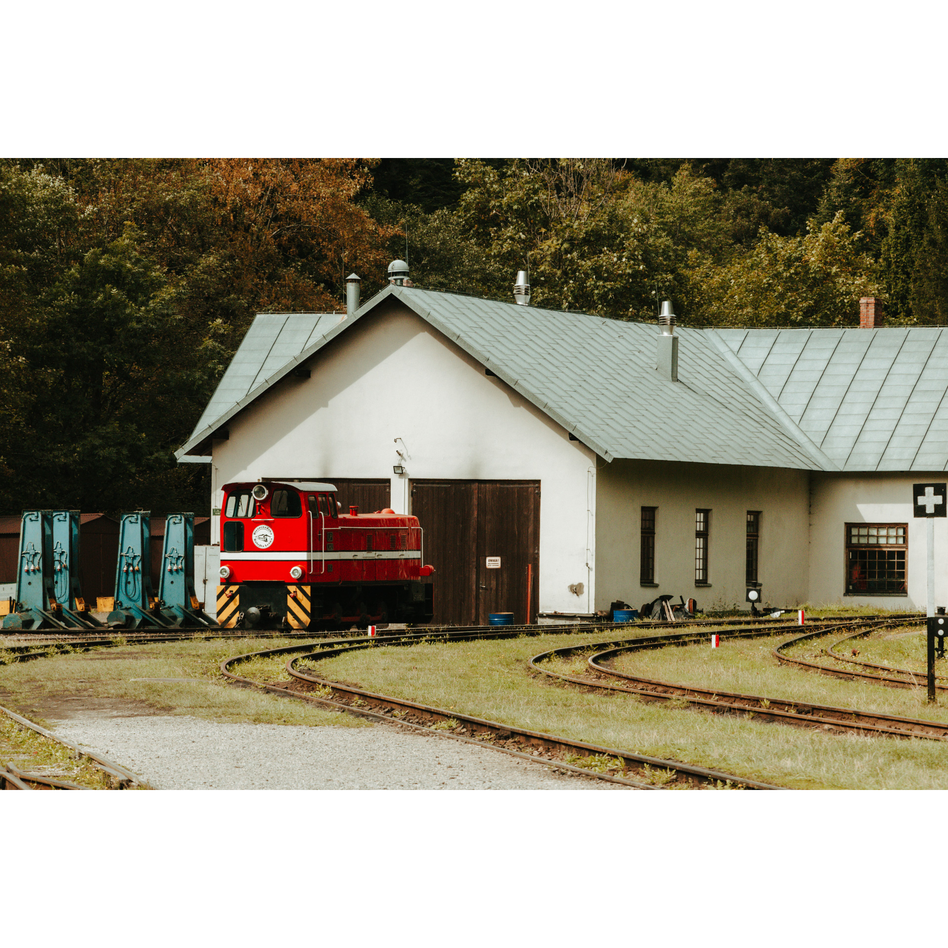 A red forest railway standing on rails in front of a white building with a gray roof