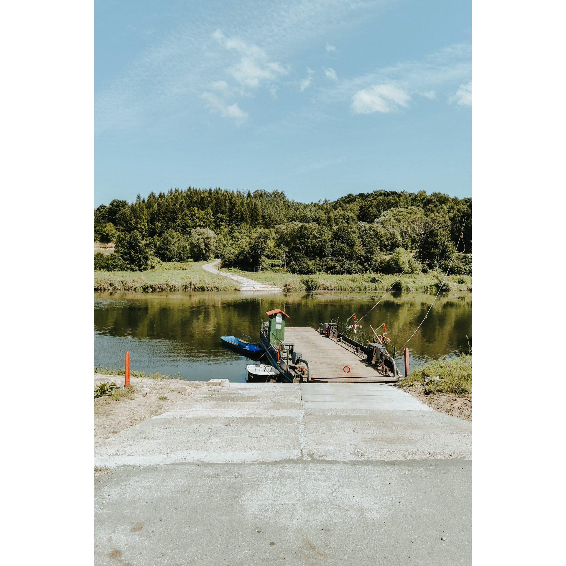 A wooden bridge on the shore of the lake overlooking the paved road and the forest on the other shore