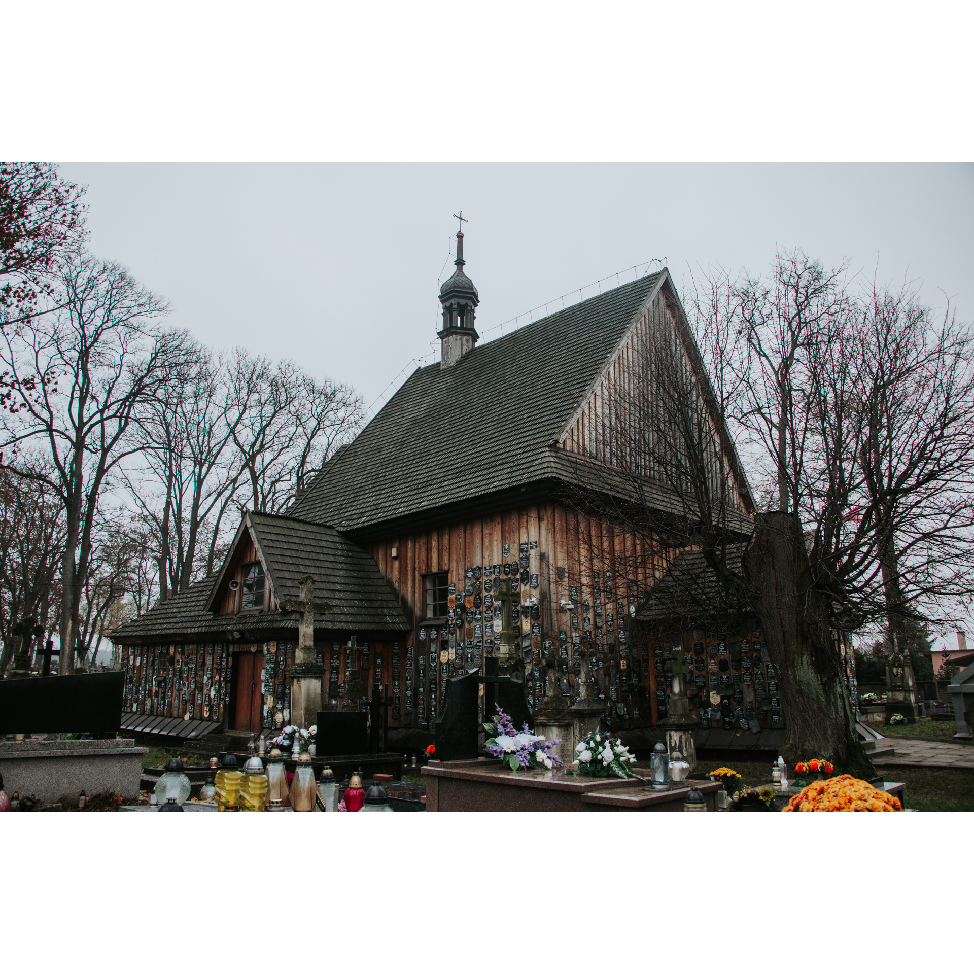 A brown cemetery chapel with a dark roof and tombstones on the walls surrounded by tombstones