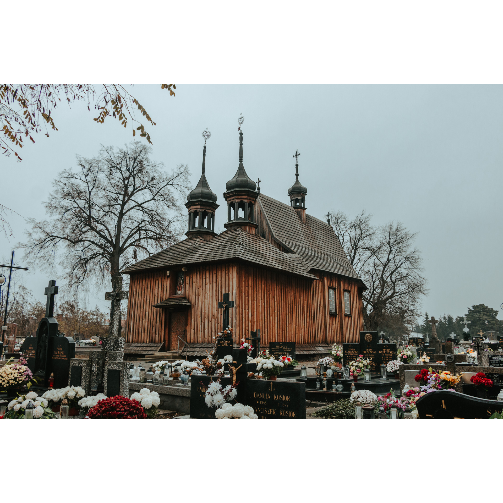 A brown, wooden cemetery chapel surrounded by dark, granite tombstones