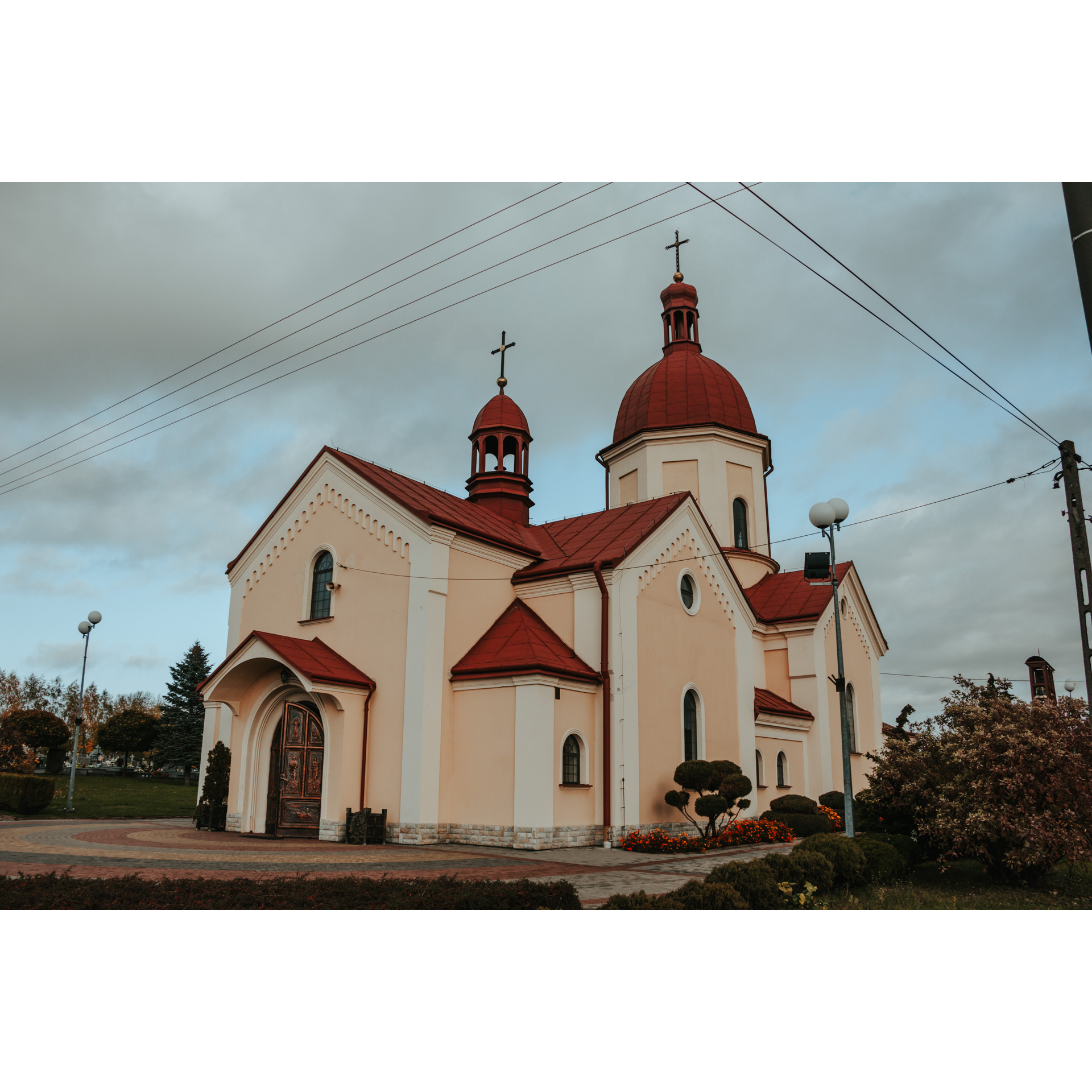 Jasnopomarańczowy kościół z czerwonym dachem i cmentarzem w tle