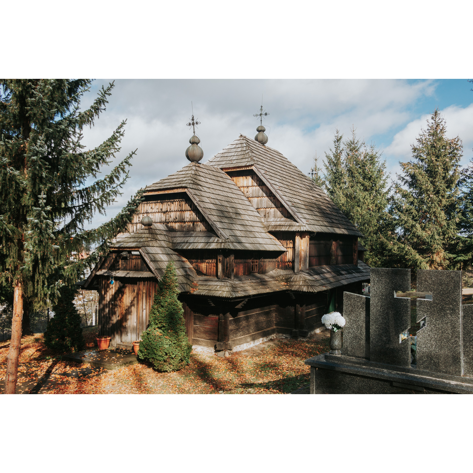 A wooden, brown Orthodox church and a concrete slab with the symbol of the Orthodox cross surrounded by coniferous trees