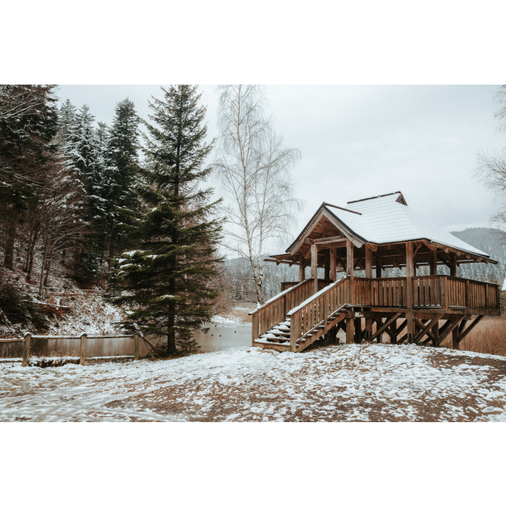 A wooden lookout shelter next to snow-covered trees and a lake