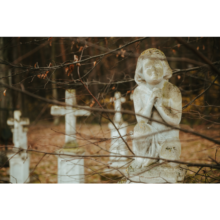 Kamienna figurka modlącego się dziecka na tle kamiennych krzyży w lesie 