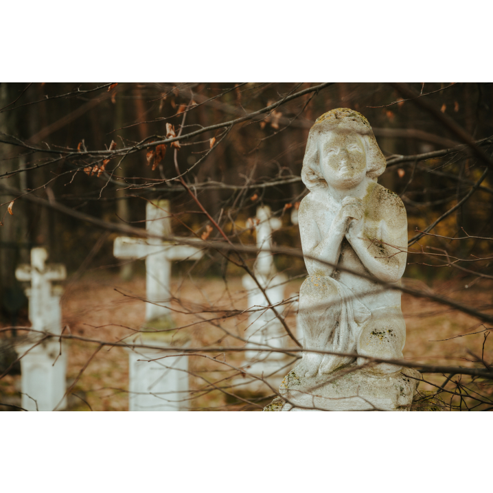 A stone figure of a praying child against the background of stone crosses in the forest