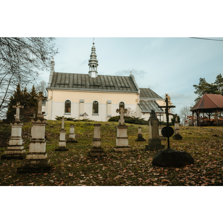 Crosses and stone cemetery shrines against the backdrop of a bright church with a gray roof and a tower