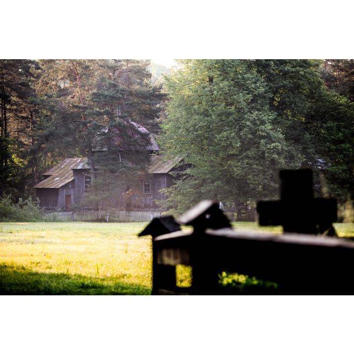 A wooden fence against the background of an old wooden church among tall grasses and trees