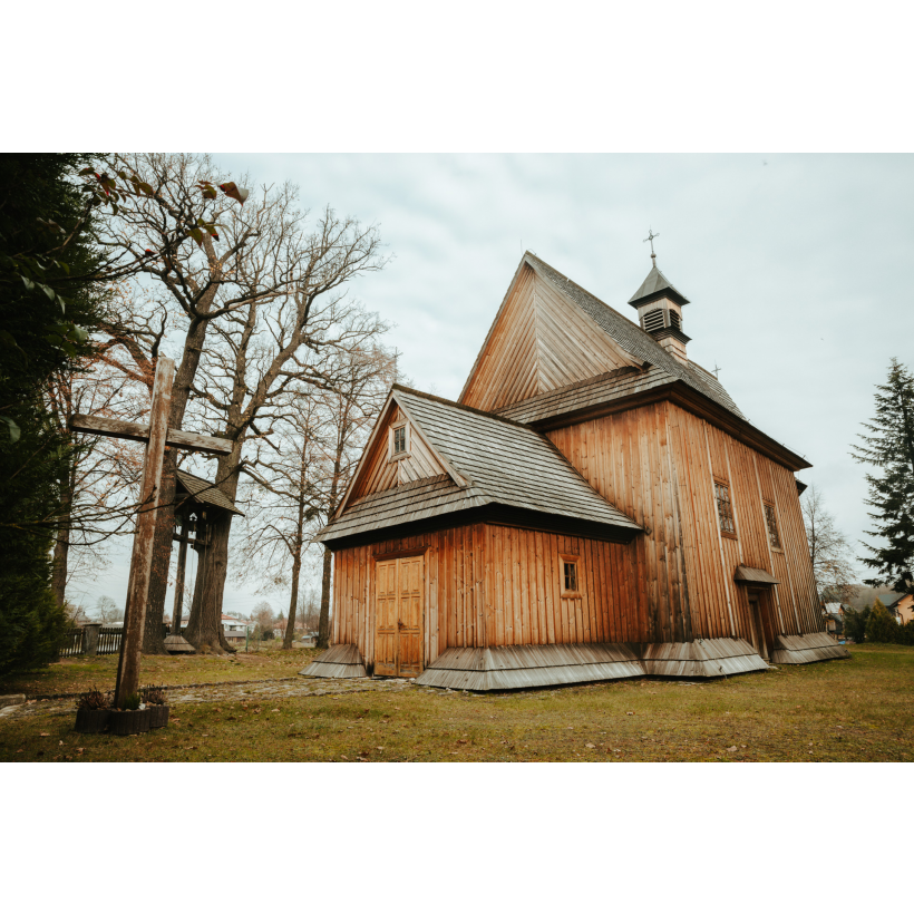 A wooden church with a two-sided sloping roof next to a tall wooden cross