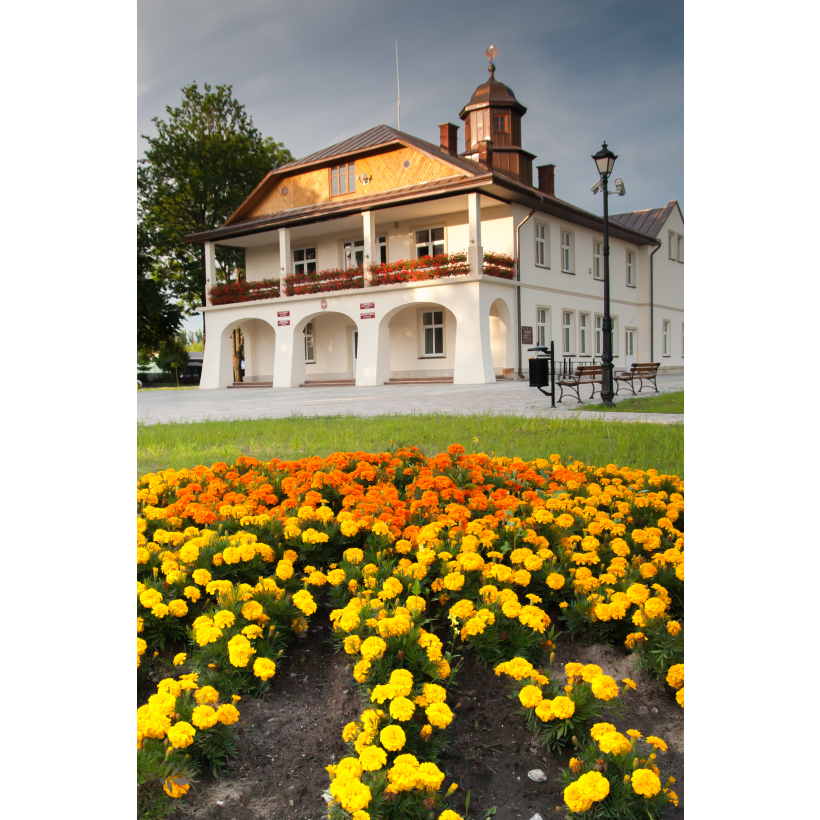 A bright building with arcades and an attic with a wooden finish, surrounded by yellow and orange flowers