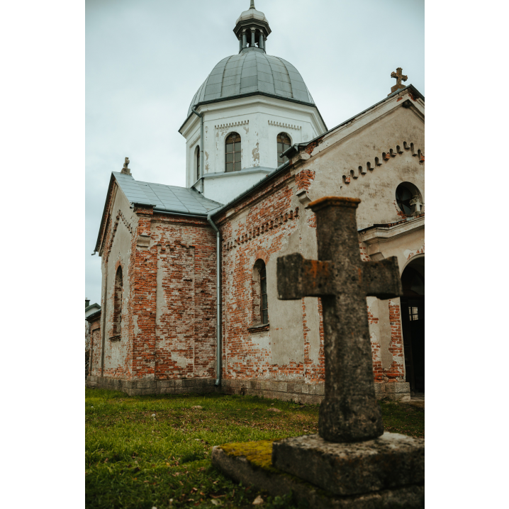 Stary, kamienny krzyż na tle murowanej, nieco zniszczonej cerkwi