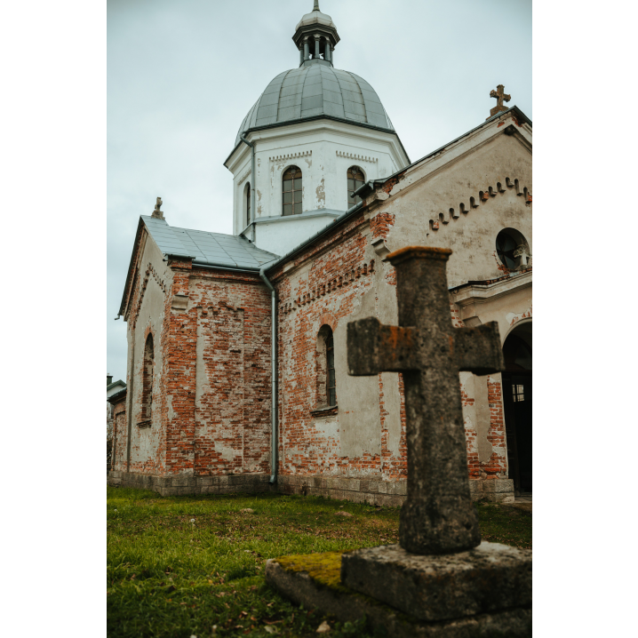 An old, stone cross against a brick, slightly damaged church in the background