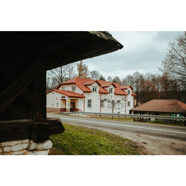 Beżowy budynek muzeum z czerwonym dachem widoczny zza drewnianego domu