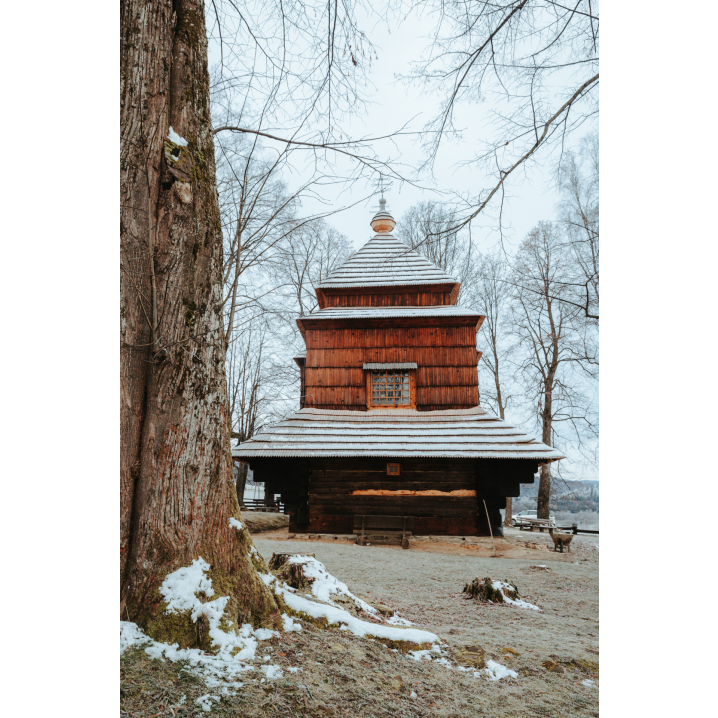 Wooden Orthodox church with a snow-covered roof and a large window among the trees