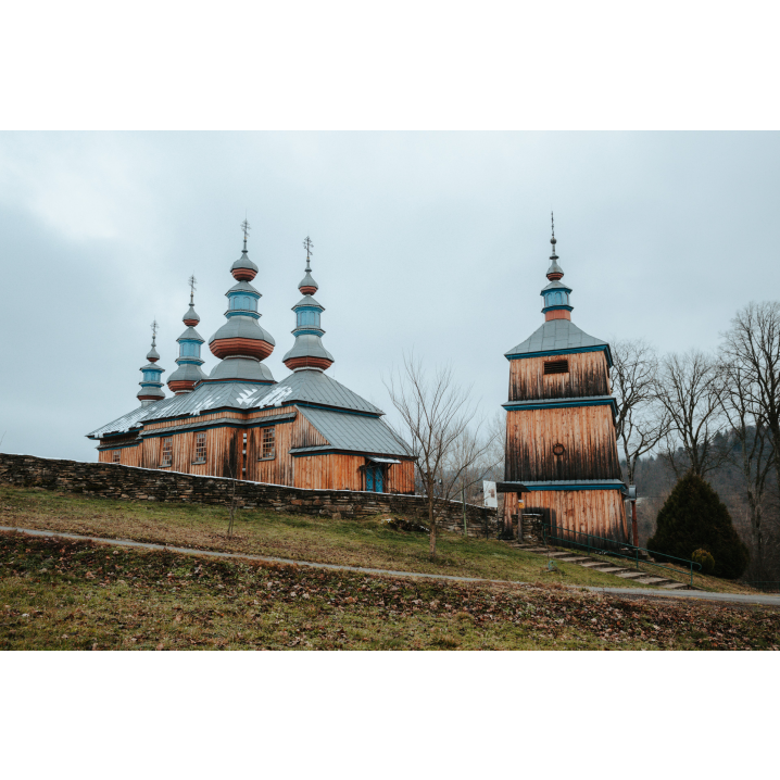 A wooden Orthodox church with soaring turrets on the roof and a wooden belfry building on the right