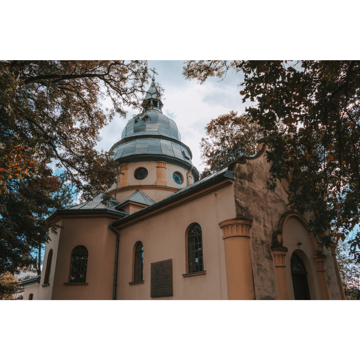 Jasnopomarańczowy budynek cerkwi wśród drzew 