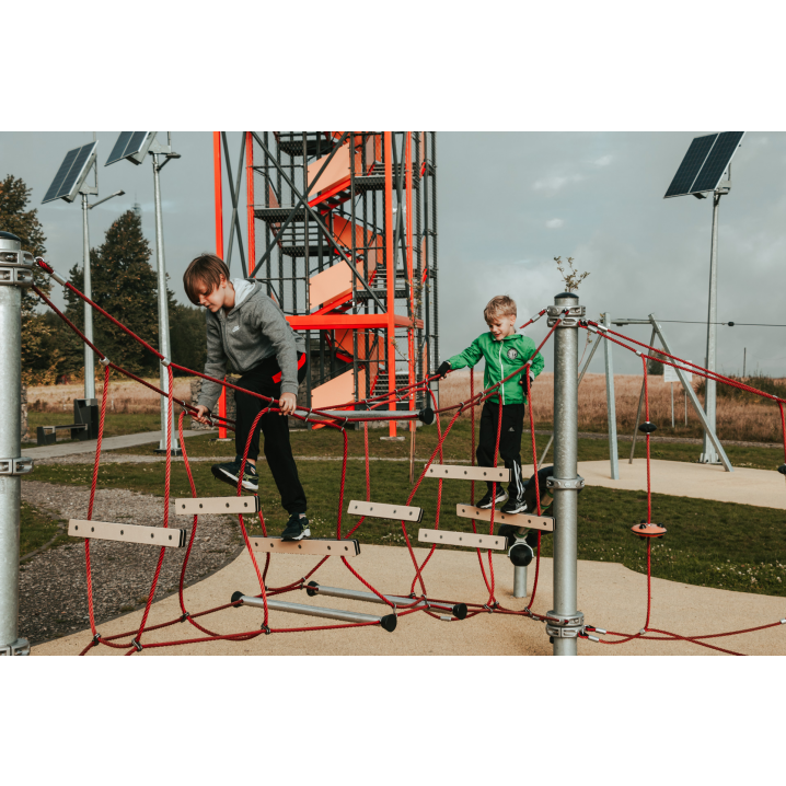 A boy in a gray sweatshirt and a boy in a green sweatshirt walking through an obstacle course made of hanging wooden tiles connected by a red string