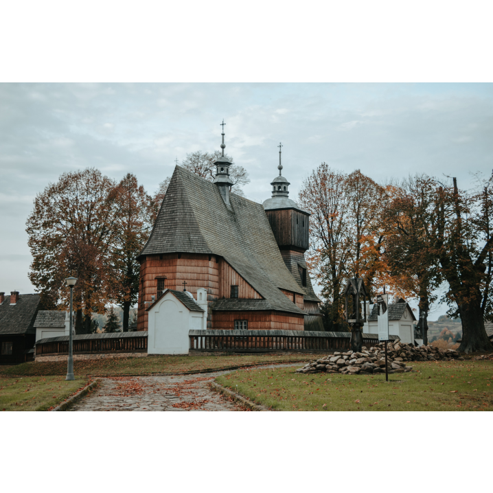 A cobbled road to a wooden church surrounded by a fence with white brick chapels