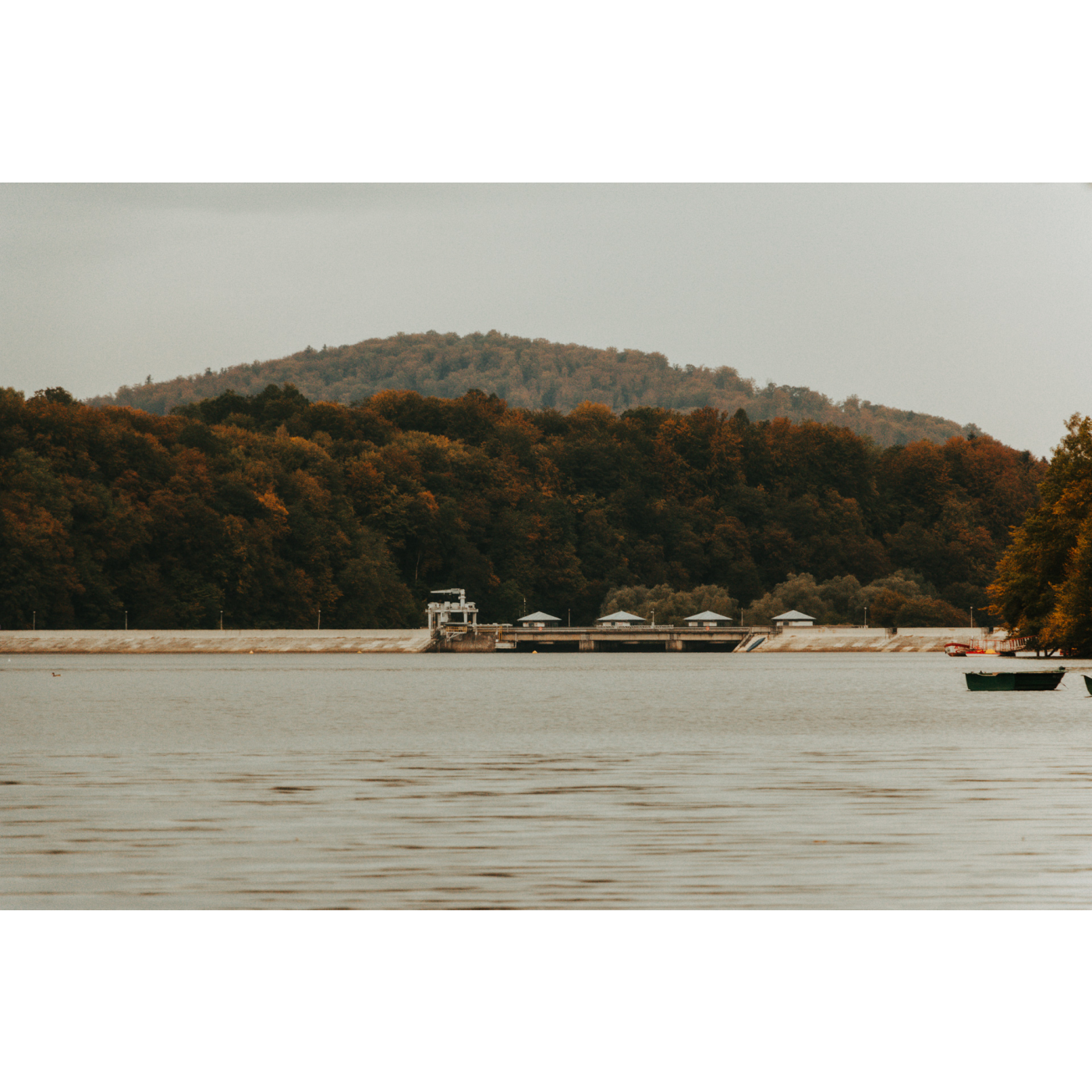 A lake with a visible dam and a panorama of forest hills