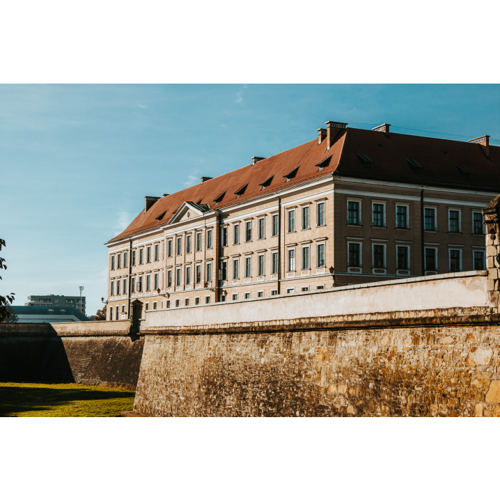 A castle with a red roof and large windows on several floors behind the wall and the moat