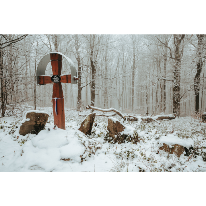 A wooden cross among snow-covered large stones in the forest