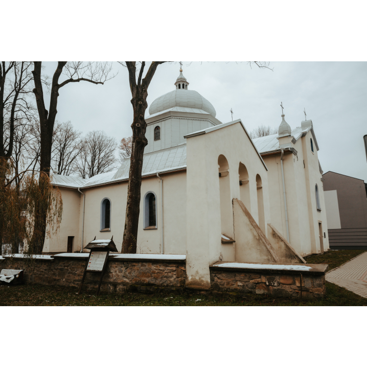 A view of a white, brick Orthodox church with a bell tower and a low stone wall