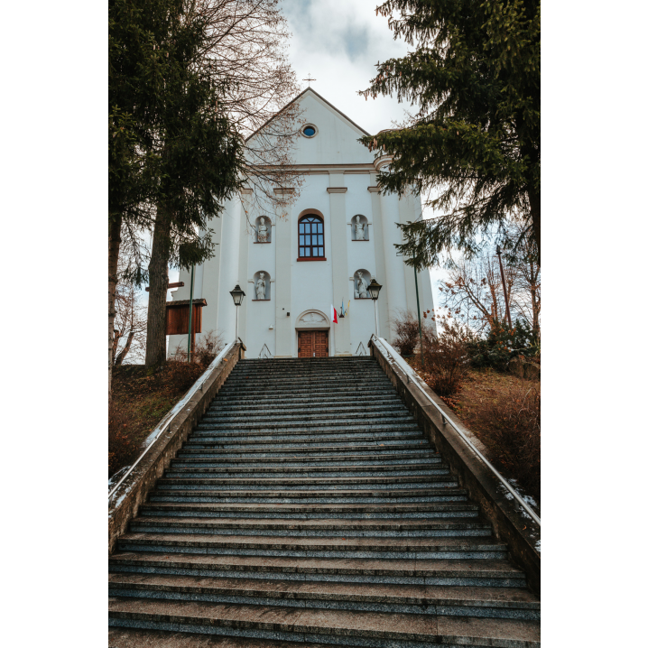 Szerokie, kamienne schody prowadzące do wejścia dużego, białego kościoła z trójkątną fasadą
