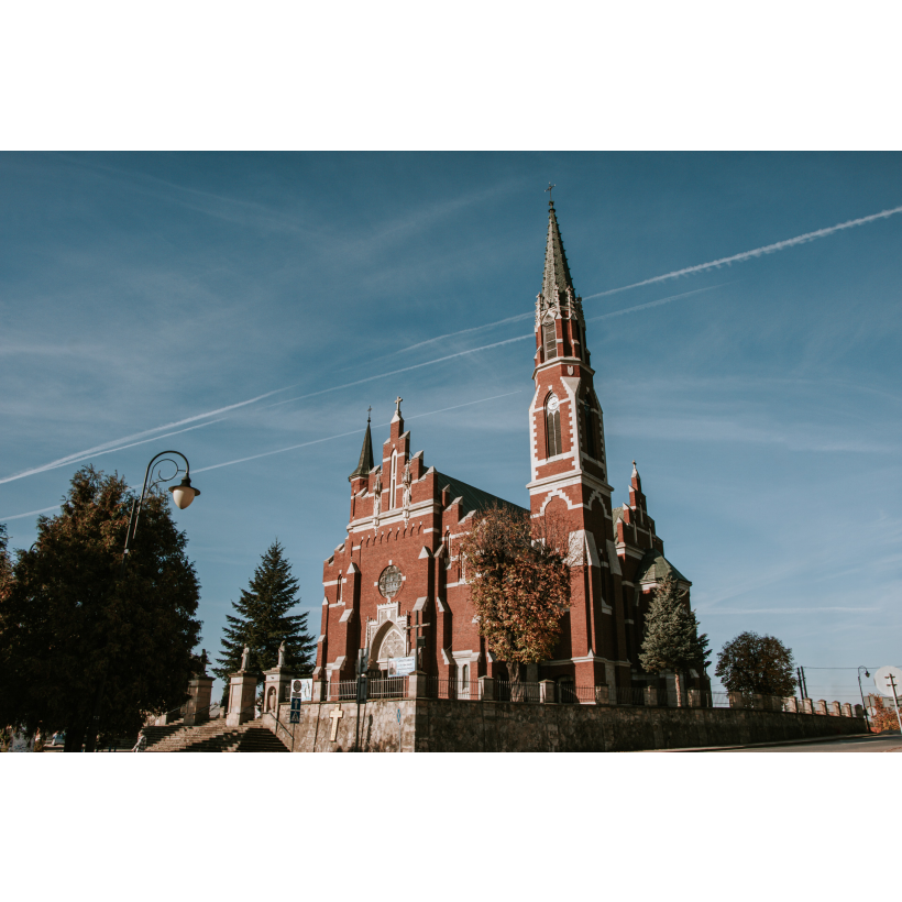 Duży ceglany kościół z białymi wykończeniami, schodkową fasadą oraz ze strzelistymi, wysokimi wieżami 