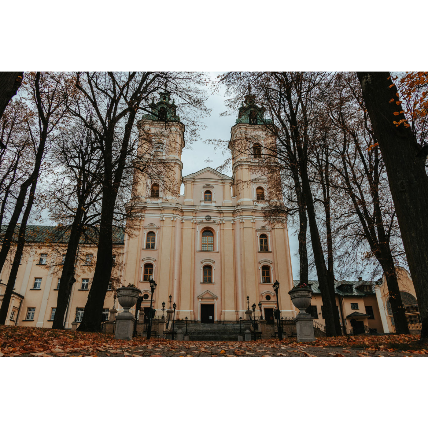 Beżowy kościół z dwoma wieżami przy fasadzie, do którego prowadzą szerokie schody wśród drzew