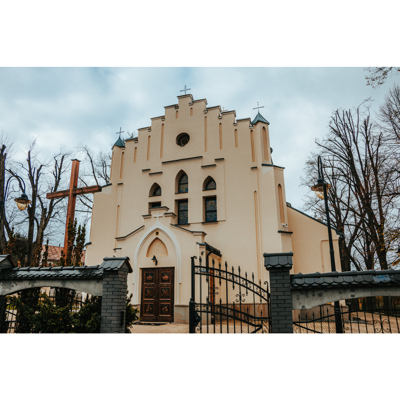 The stepped facade of a light beige church with three oblong windows next to a wooden cross