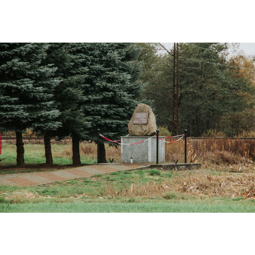 An erratic boulder with a commemorative plaque attached, set on a low pedestal next to coniferous trees