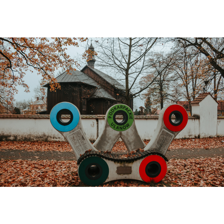 A bench in the shape of a bicycle chain against the background of a small wooden church