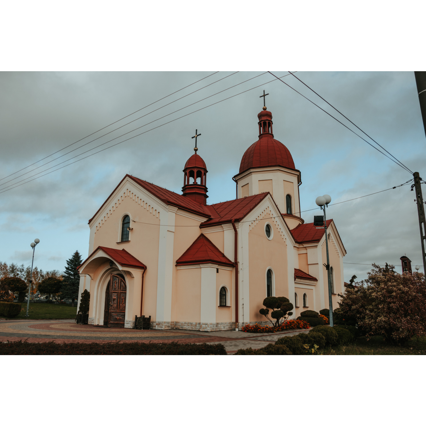 A pale salmon colored brick church with a contrasting dark orange roof, two domes, and a door with painted paintings