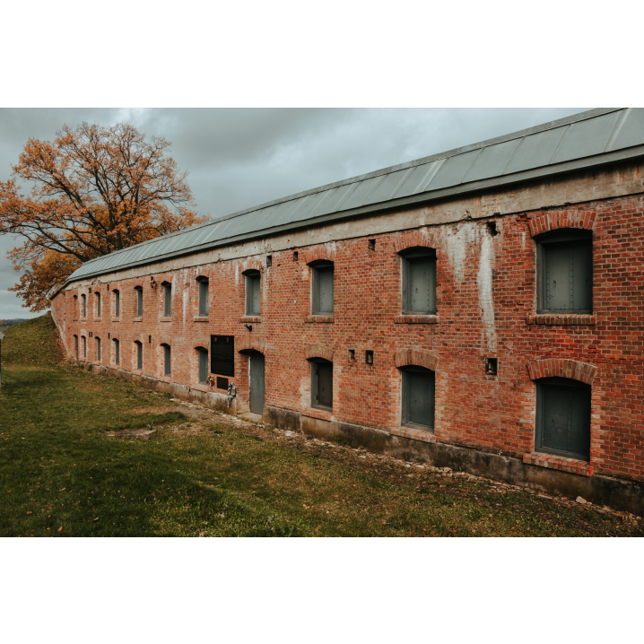 Long red brick buildings with evenly spaced arched openings resembling windows, the whole thing is surrounded by small hills covered with grass and trees