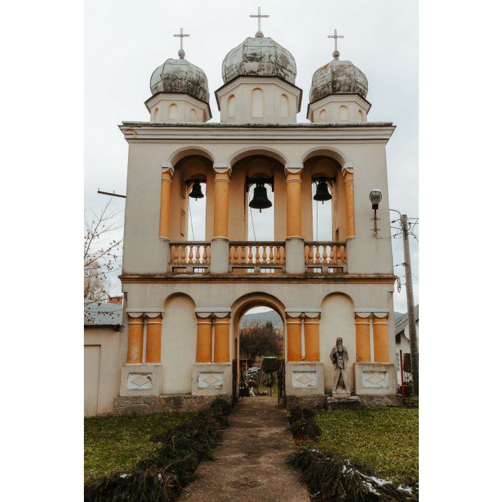 A brick bell tower in beige and salmon colors with three arcades, which are topped with onion-shaped domes and crosses