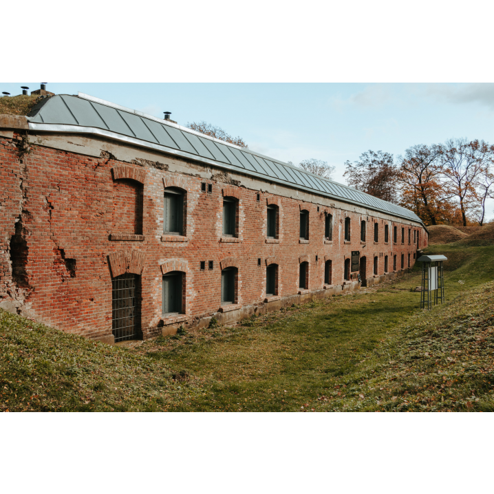 Long red brick buildings with evenly spaced arched openings resembling windows, the whole thing is surrounded by small hills covered with grass and trees