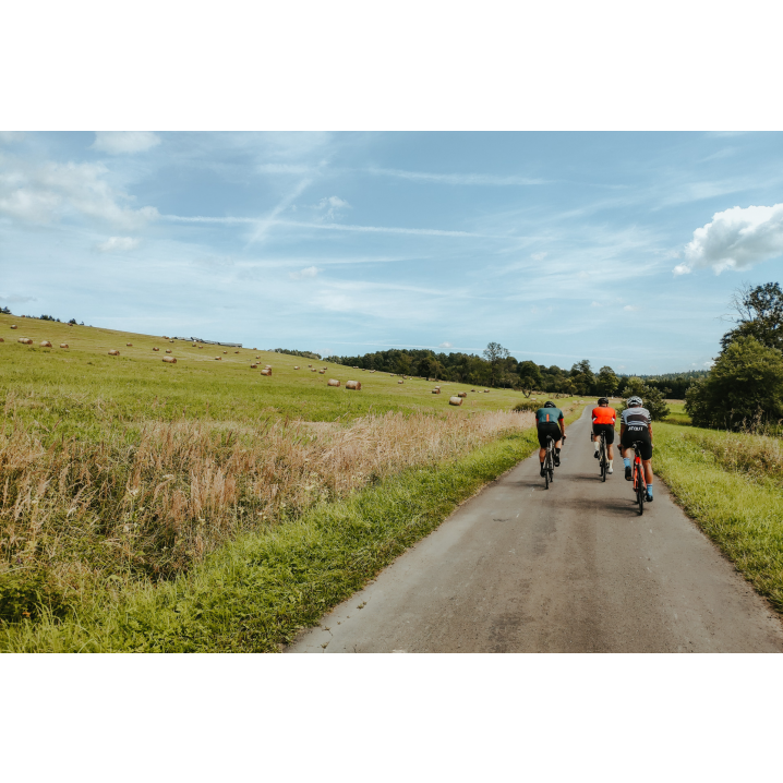 Three cyclists riding a gravel road between fields with haystacks