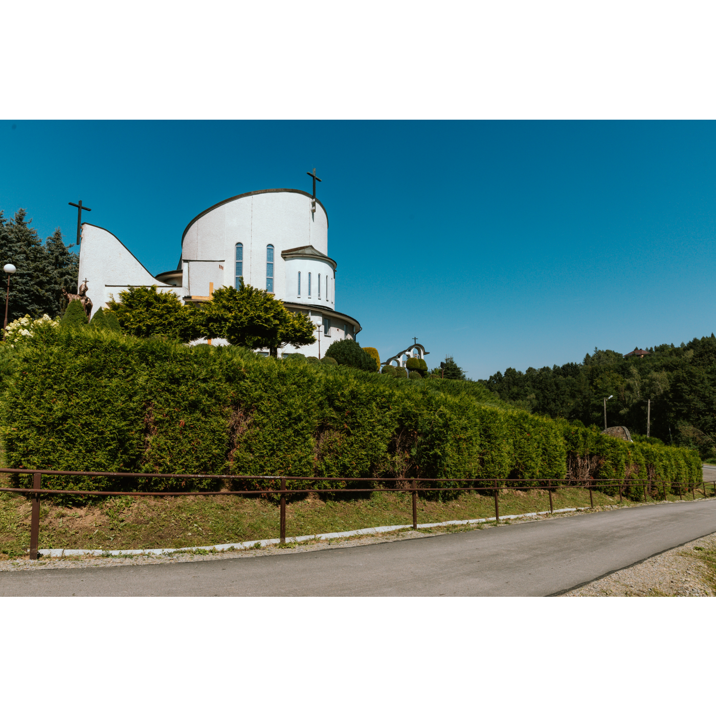 Semicircular facade of a white church on a hill, green vegetation at the bottom, blue sky in the background