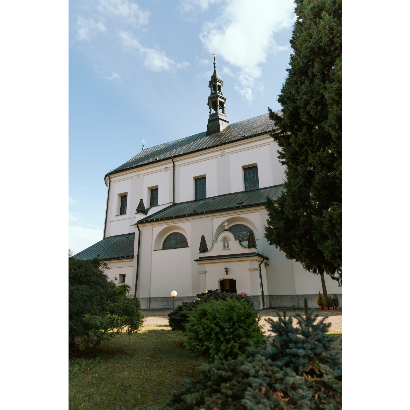 The side of the church with light walls, rectangular and semi-circular windows and a small, soaring tower